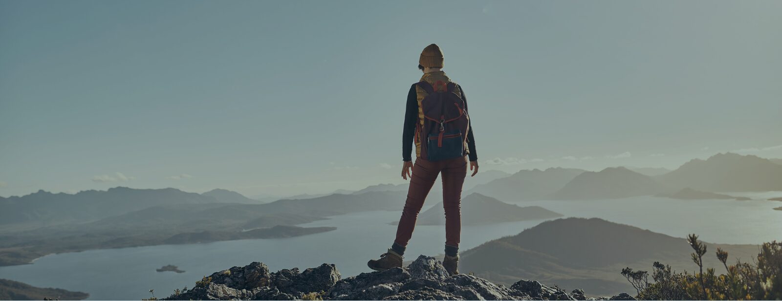Woman hiker standing atop a peak overlooking a vast open landscape with a large lake