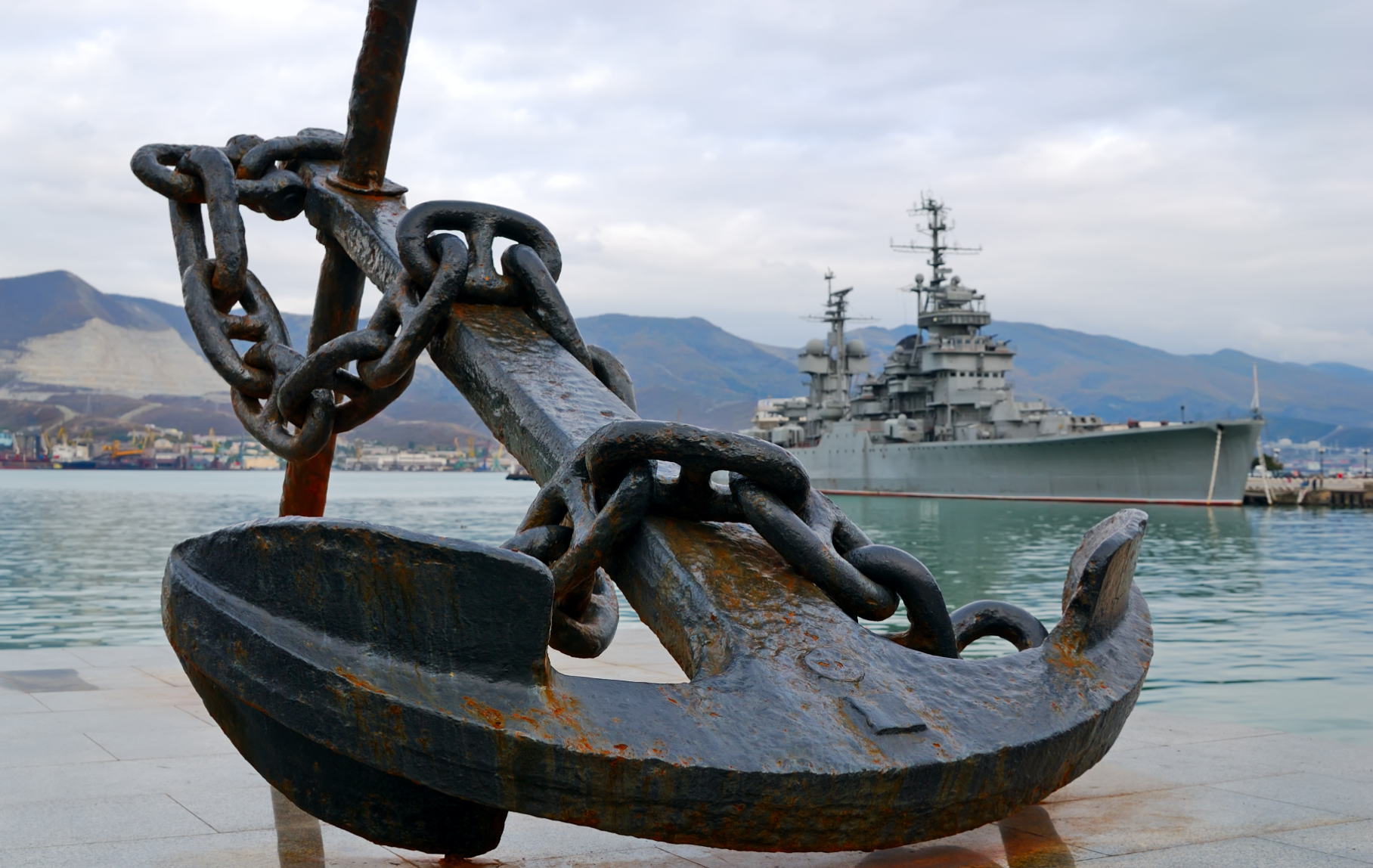 photograph of a large anchor on the shore with a ship in the background